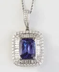 Platinum Pendant, with an emerald cut 13.87 carat tanzanite atop a border of baguette diamonds and an outer border of round diamonds, with a diamond m