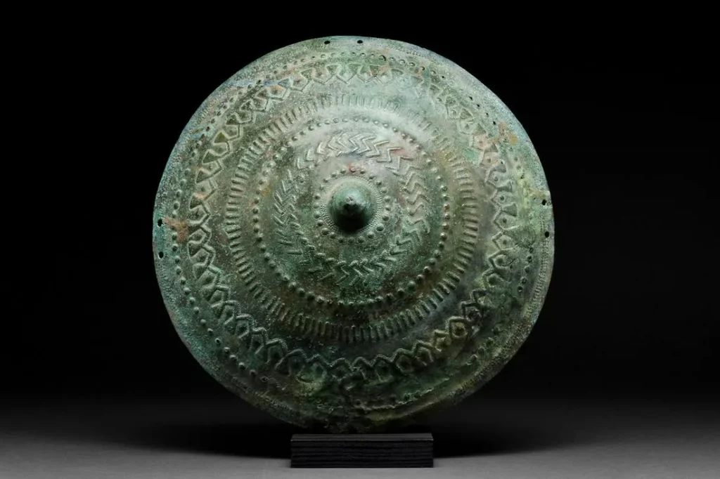 Rare Urartu (Iron Age kingdom in the historic Armenian highlands) convex bronze shield tondo with carinated, conical center. Decorated in repousse and ornamented with bosses, zigzags, vertical bars, arches. Circa early 1st millennium BC. Provenance: property of a London gentleman. Believed to have been previously part of Axel Guttman collection. Estimate £10,000-£15,000 ($12,545-$18,820)