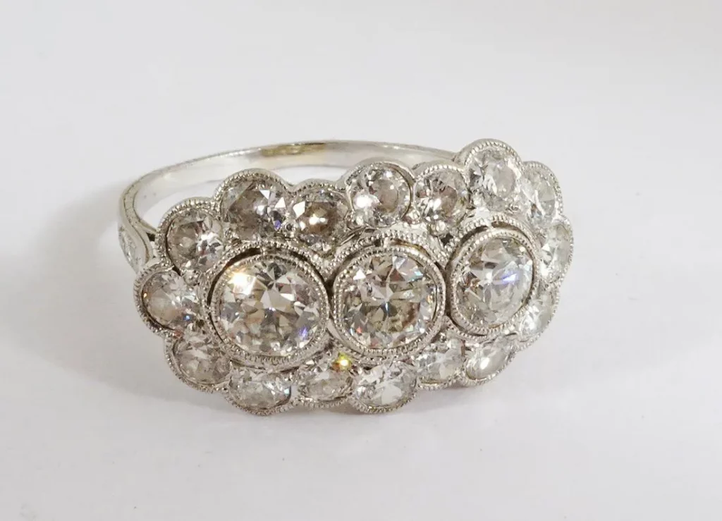 Platinum cluster ring with antique mounting that features three large round diamonds (each 4.2-4.5mm, 1.00 cttw) surrounded by 16 early-cut round accent diamonds (2.00 cttw) scalloping the perimeter of the main stones. Estimate $1,500-$2,500