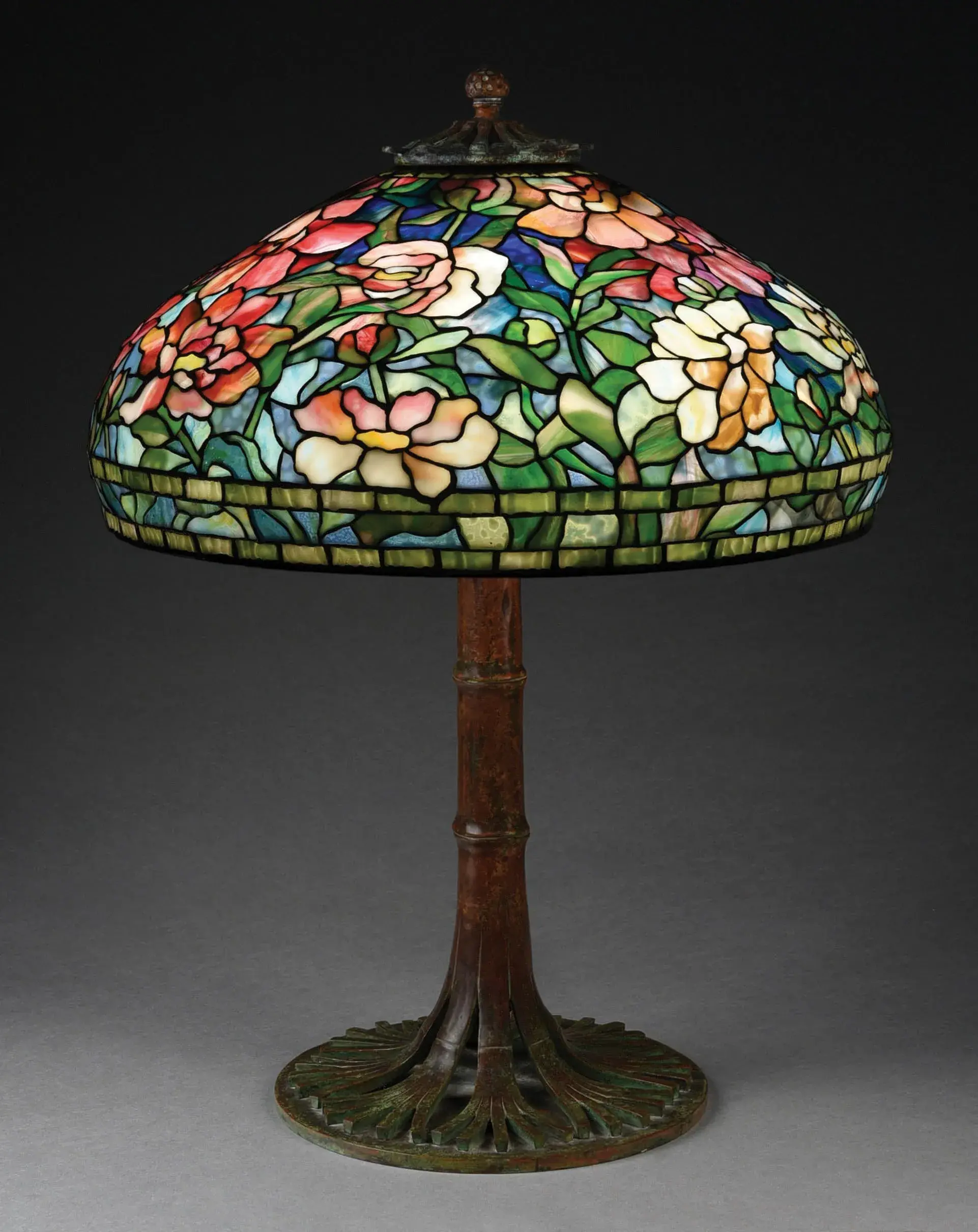 Tiffany Studios ‘Peony’ leaded-glass lamp with multicolored background of mottled cobalt blues and streaked sky blues. Extensive multicolored confetti glass with wonderful transparency. Blossoms comprising numerous types of Tiffany glass, including granite-backed reds and highly mottled opalescent whites. Shade and base are signed by Tiffany. Provenance: shade formerly in Minna Rosenblatt collection; base previously sold at Sotheby’s. Sold within estimate range for $110,700