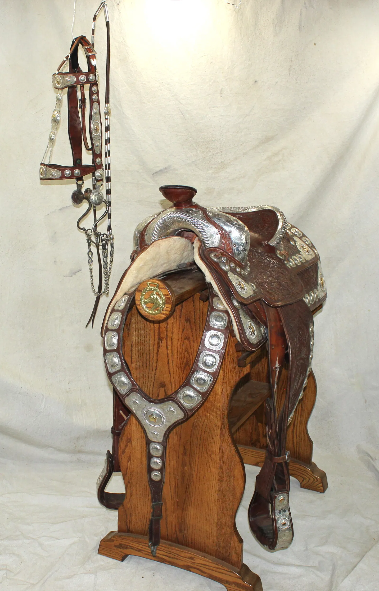 Pat Gill fully silver-mounted saddle with matching bridle and martingale. Profusely carved with floral motif throughout and heavily adorned with engraved silver. Details include silver-lined perimeters, bound and rope-edged cantle and gold horsehead swells, horn cap and stirrups; and detailed corner plates accented by gold stars. Martingale covered in 21 detailed and engraved square silver conchos, the chest plate having a central gold star. Near mint. Estimate: $10,000-$14,000
